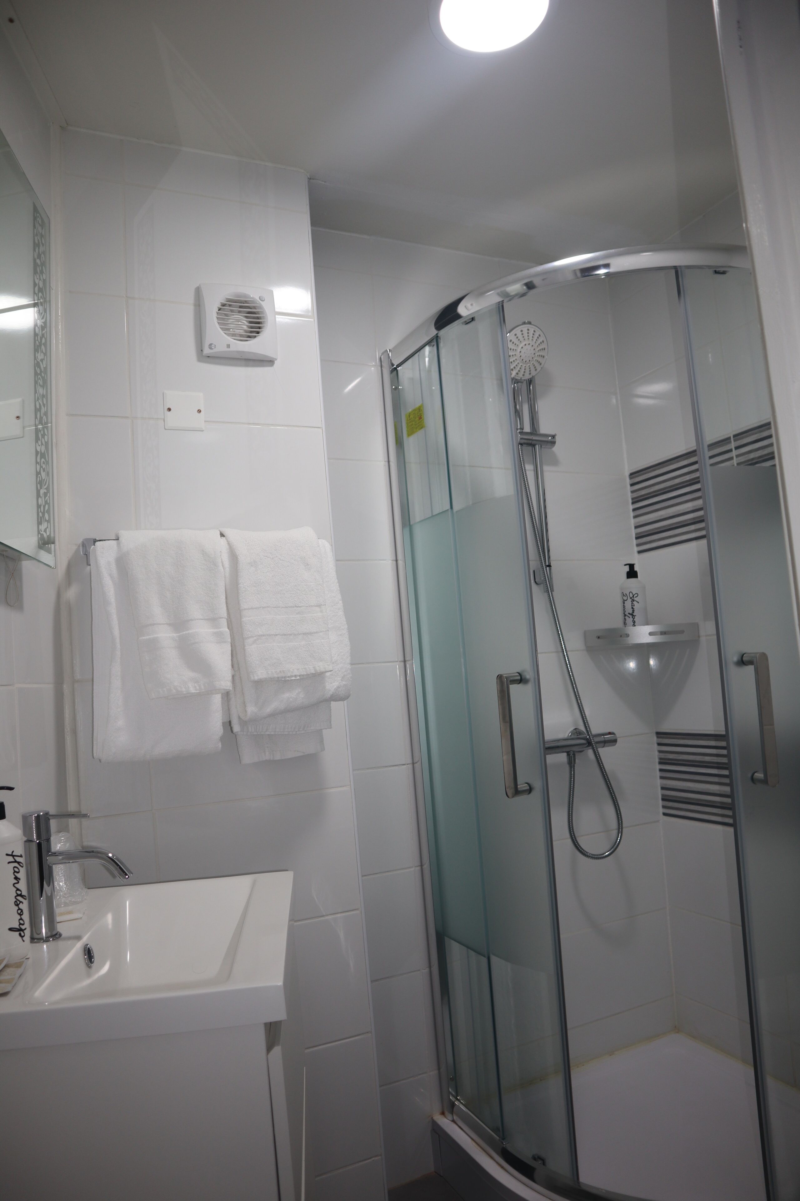 Ein modernes Badezimmer mit einer gläsernen Duschkabine, einem weißen Waschbecken und zwei Handtüchern, die an der Wand hängen.