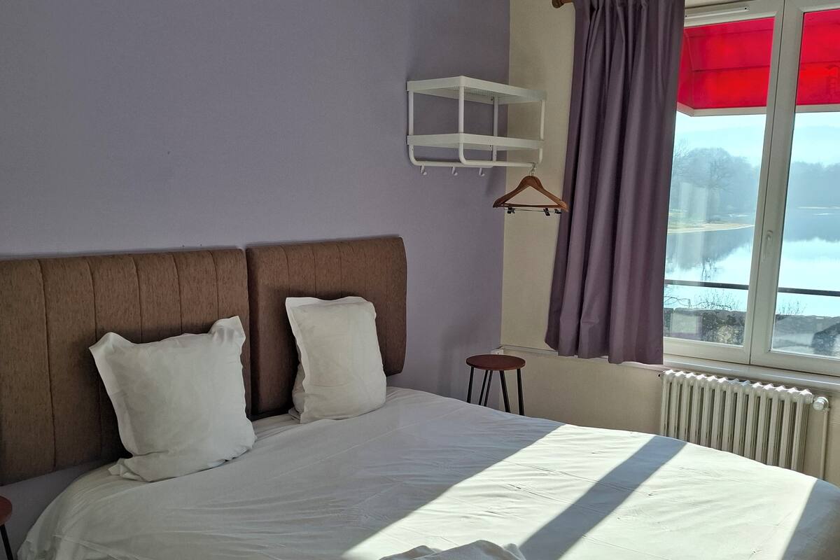 A neatly made bed with white linens, a headboard, and a window with curtains.