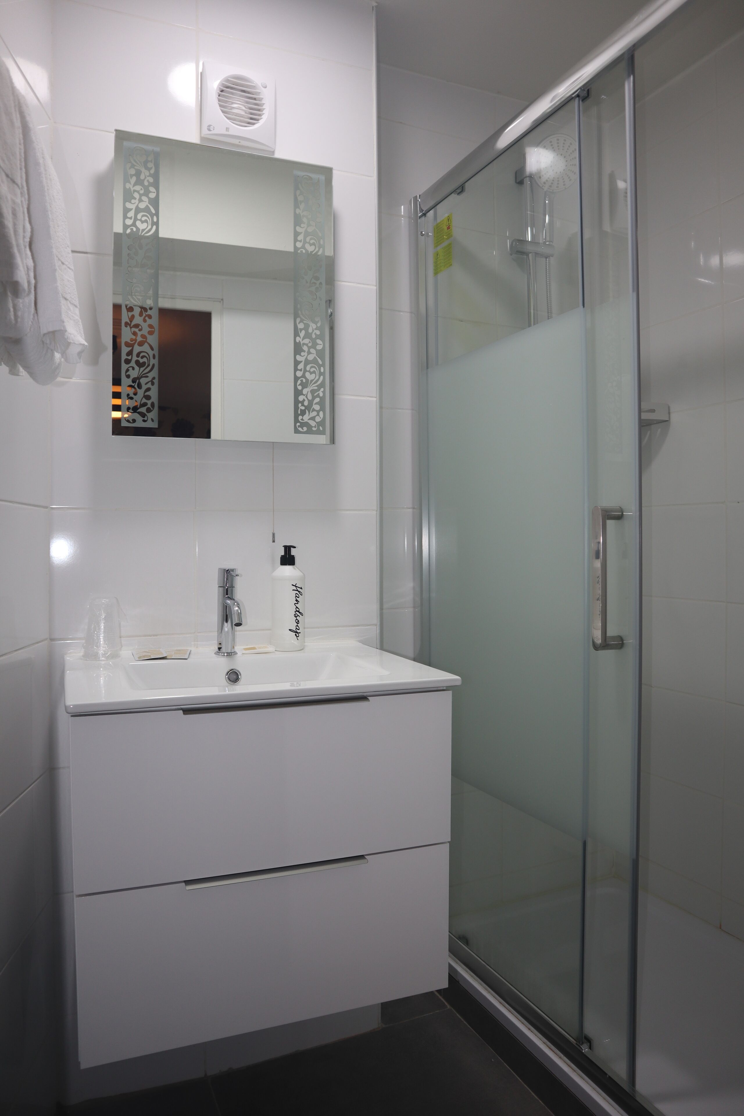 A modern bathroom with a glass shower enclosure, a white vanity with a mirror, and a hand dryer.