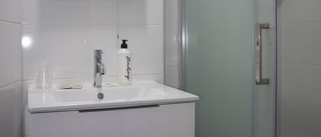 A modern bathroom with a glass shower enclosure, a white vanity with a mirror, and a hand dryer.
