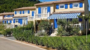 Een rij Mediterrane villa's met blauwe luiken, witte balkons en een gestreepte luifel.