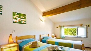 Een kamer met twee bedden, houten hoofdborden, een raam met uitzicht op groen en een wandlamp.