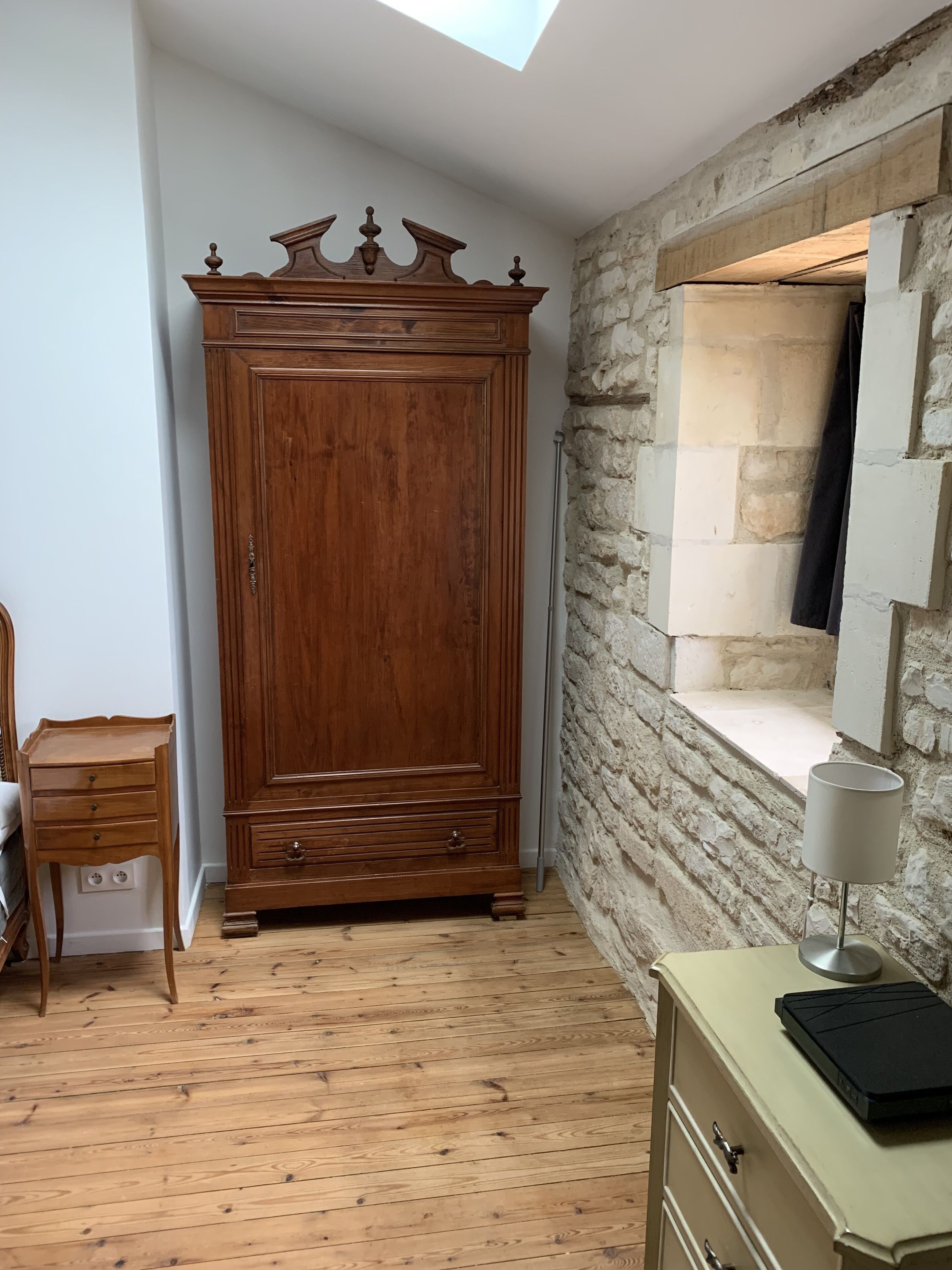 Una habitación con un armario de madera, un escritorio pequeño, una lámpara y una pared de piedra.