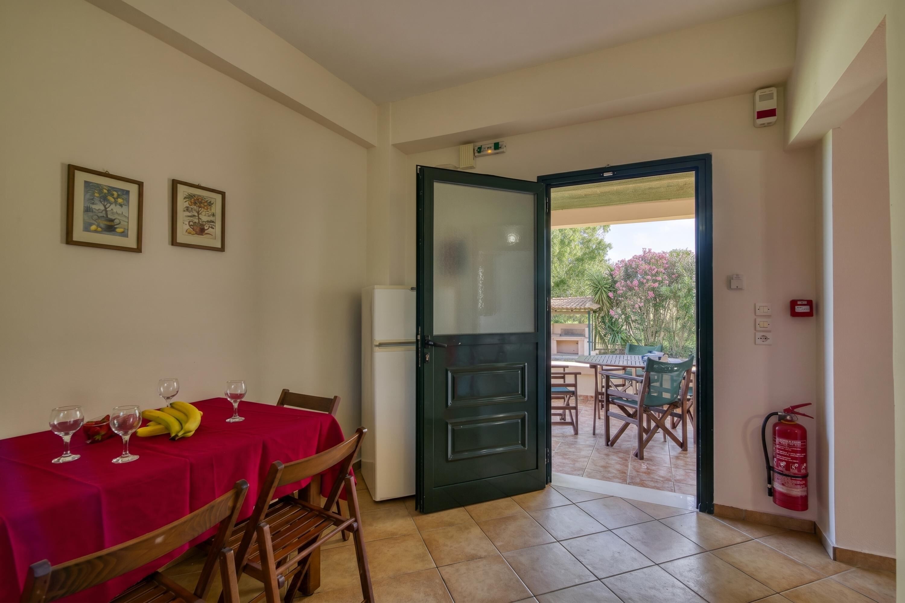 Comedor con una mesa dispuesta para dos personas, un refrigerador y una puerta que da a un patio exterior.