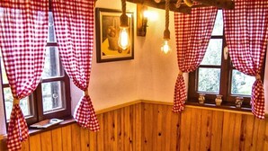 Ein gemütliches Zimmer mit Holzvertäfelung, einem Tisch mit kariertem Tischläufer und roten und weißen Karottenvorhängen.