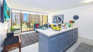 A modern kitchen with a large island, a dining area with a blue sofa, and a view of high-rise buildings.