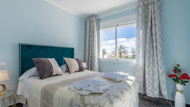 A hotel room with a bed, a window with curtains, a vase with flowers, and a nightstand with a lamp. - Villa 'Galicia' with Mountain View, Private Pool and Wi-Fi (Calpe)