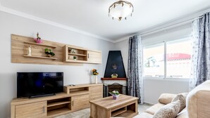 A living room with a flat-screen TV, wooden entertainment unit, sofa, coffee table, fireplace, and a large window with curtains. - Villa 'Galicia' with Mountain View, Private Pool and Wi-Fi (Calpe)