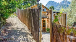 Une porte en bois rustique qui mène à un bâtiment en pierre, orné d’une cloche et d’un pot de fleurs.