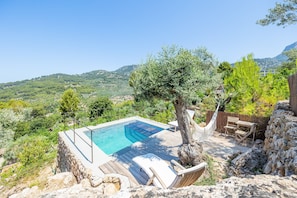 A pool with a wooden deck, a hammock, and a view of the surrounding landscape.