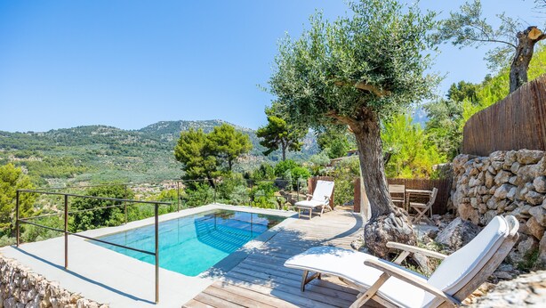 Une piscine entourée d’une terrasse en bois, dotée de chaises longues et offrant une vue sur la campagne.