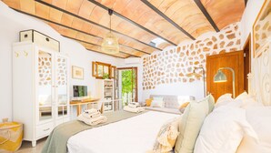 Une chambre avec un grand lit, une armoire, un bureau et un mur en pierre.