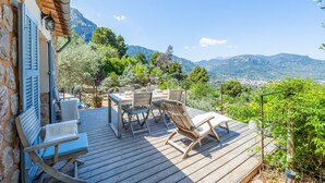 Une terrasse en bois avec des meubles d’extérieur, un mur en pierre et une vue sur les montagnes.