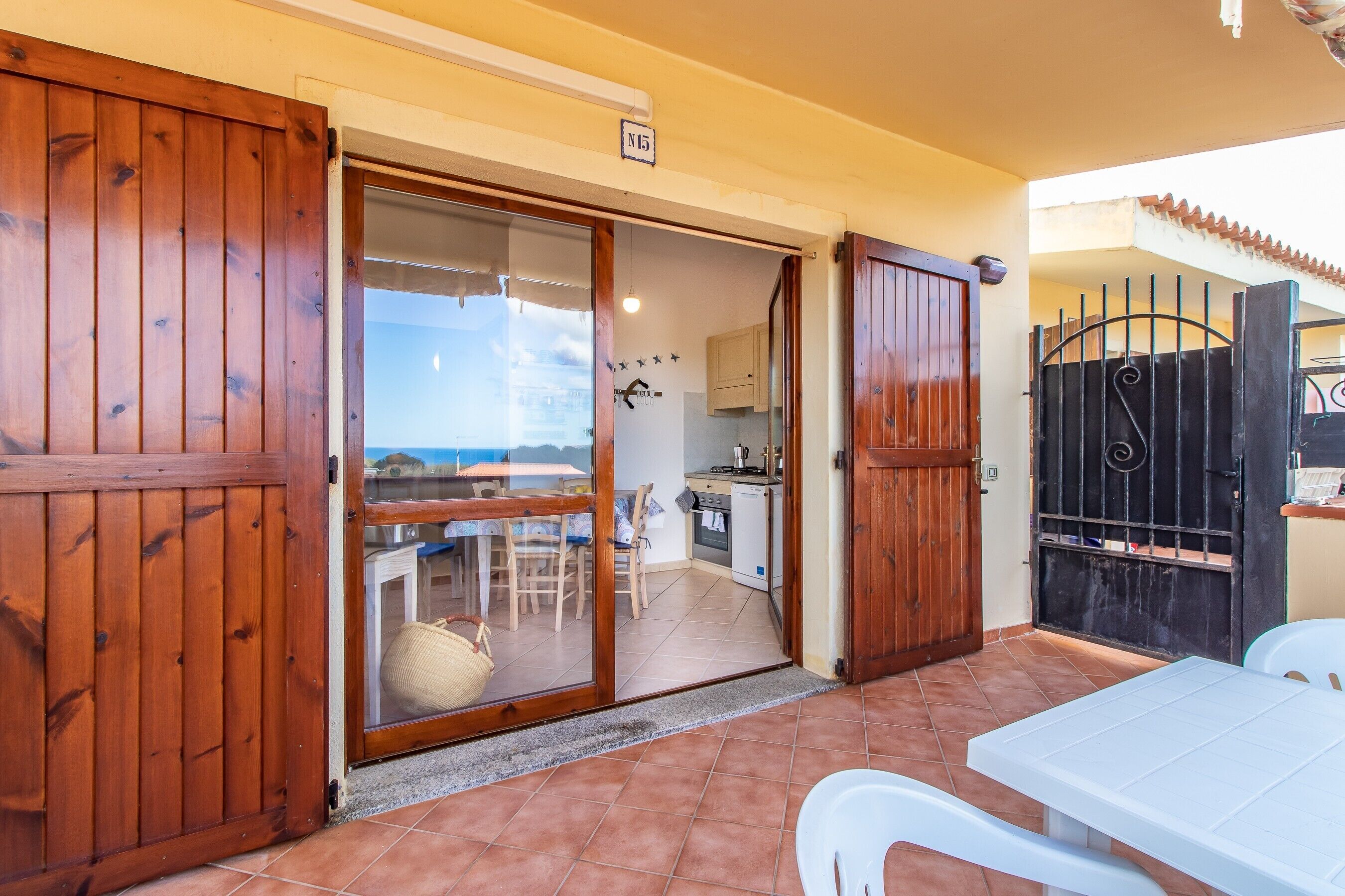 Un cancello in legno, una porta scorrevole in vetro, un tavolo bianco e un angolo cottura.