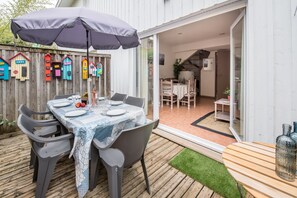Une terrasse extérieure avec une table dressée pour le repas, un parasol et une plateforme en bois.