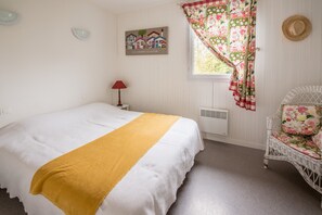 Une chambre à coucher avec un lit, une fenêtre avec des rideaux, une chaise et un tableau accroché au mur.