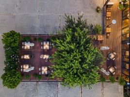 Vista aérea de un patio en la azotea con varias zonas de estar, rodeado de vegetación y un muro de piedra.