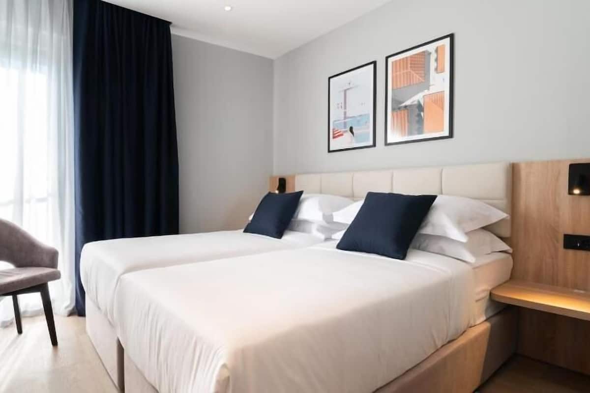 A hotel room with a large bed, a chair, a bedside table, and two framed pictures on the wall.