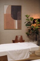 Un cuarto de spa con una mesa de masajes, una silla, una planta en maceta y una obra de arte colgada en la pared.