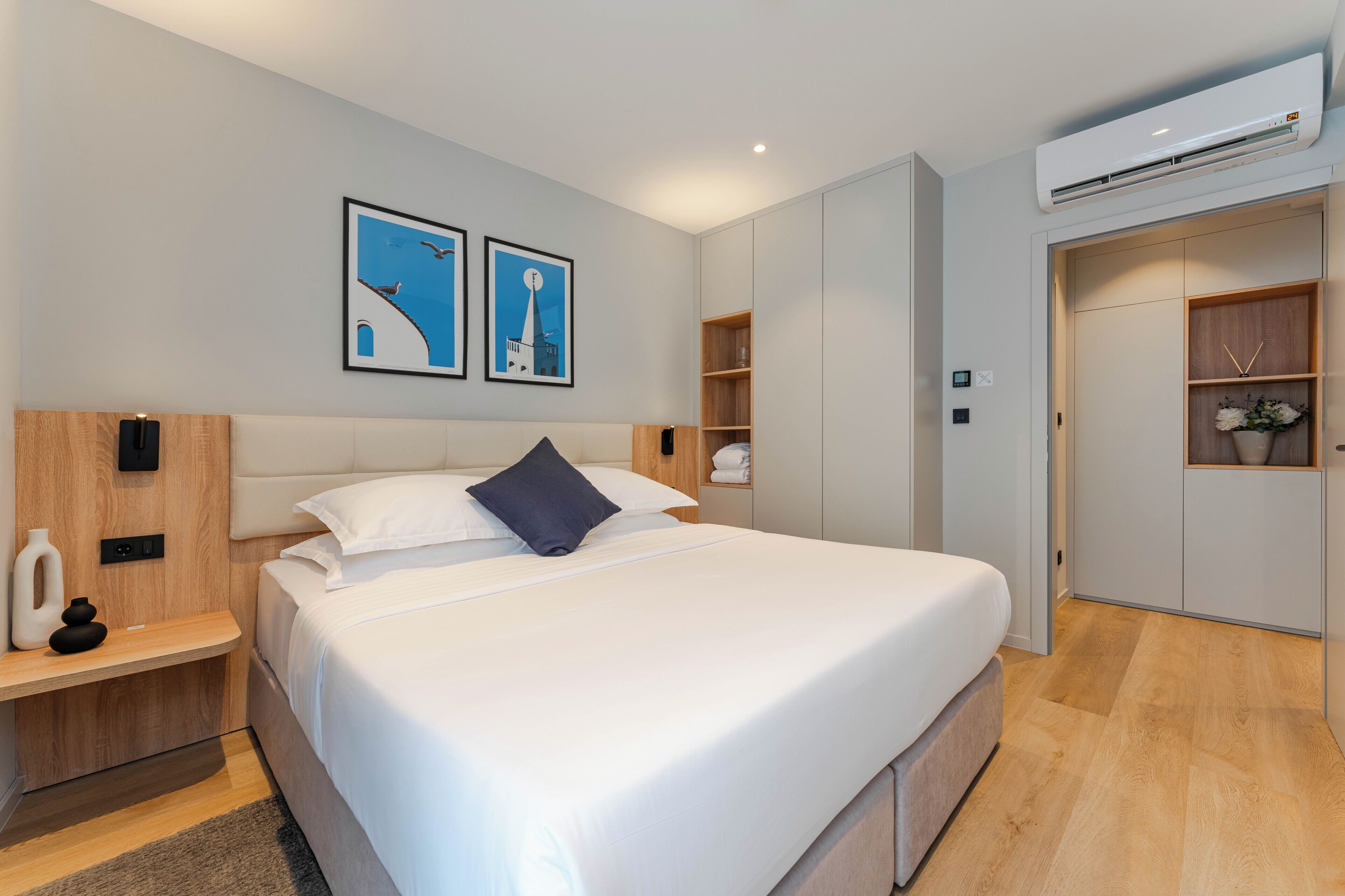 A modern bedroom with a large bed, a nightstand, a wardrobe, and two framed pictures on the wall.