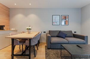 A modern living room with a grey sofa, a wooden dining table with chairs, and a coffee machine.