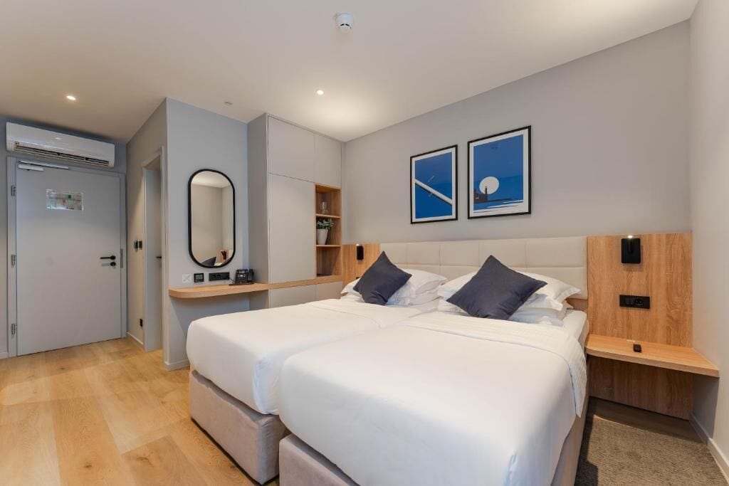 A modern hotel room with a large bed, bedside tables, a wardrobe, and a mirror.