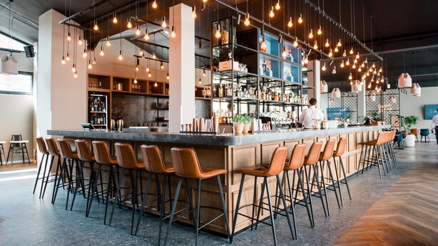 Una zona de bar moderna con una barra larga, varios taburetes y lámparas colgantes.
