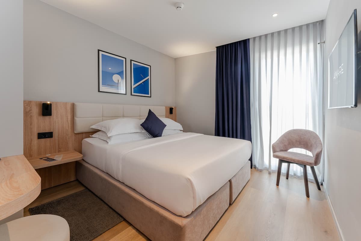 A modern hotel room with a large bed, a bedside table, a chair, and a large window with curtains.