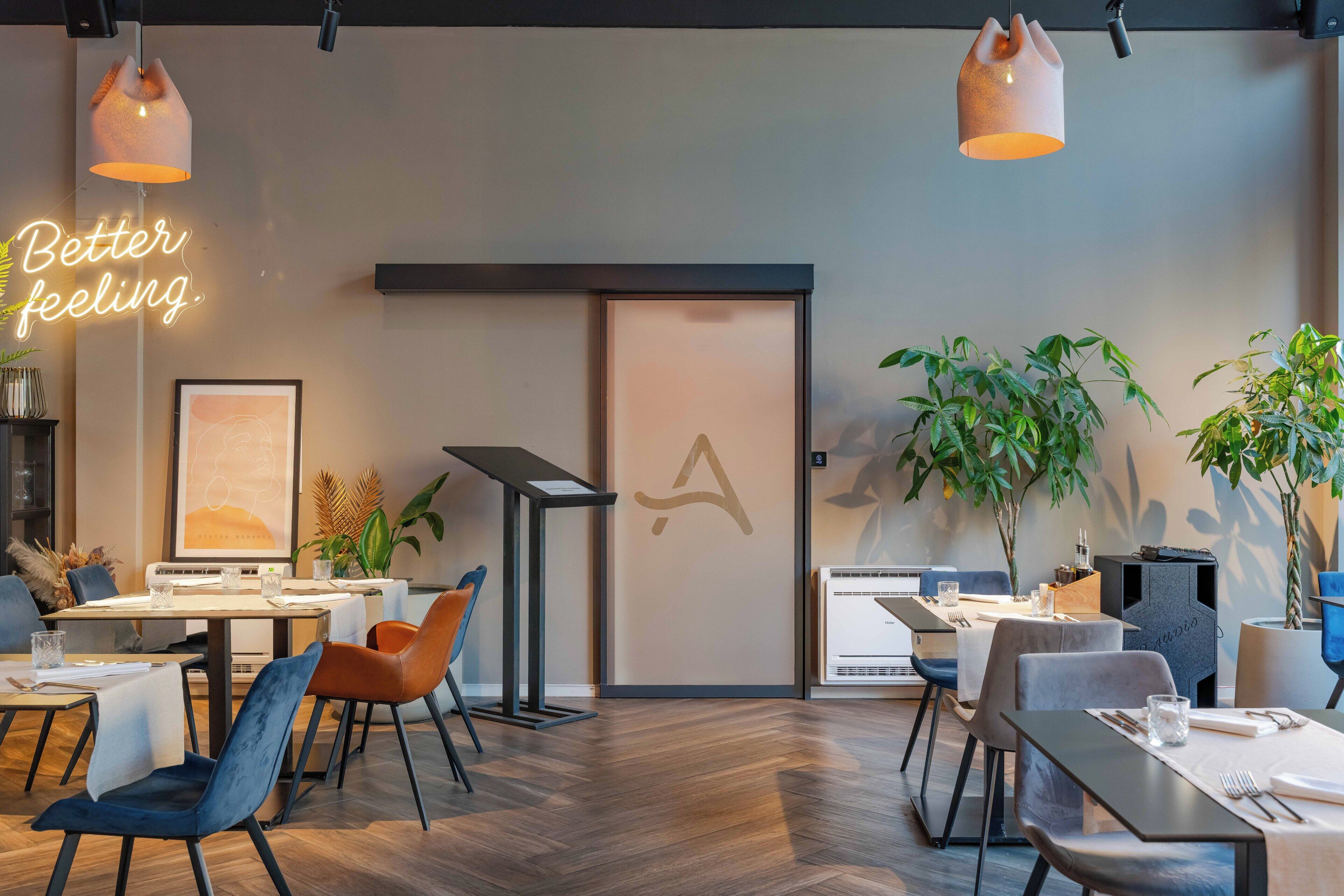 Un espace repas moderne avec des tables, des chaises, des luminaires suspendus et des plantes en pot.