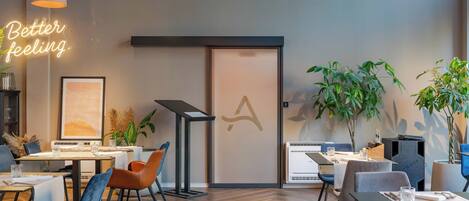 A modern dining area with tables, chairs, pendant lights, and potted plants.
