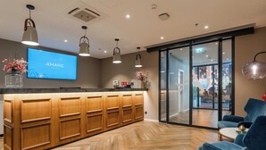 Un mostrador de recepción con pantalla de televisión, paneles de madera, iluminación colgante y vistas al interior del hotel.