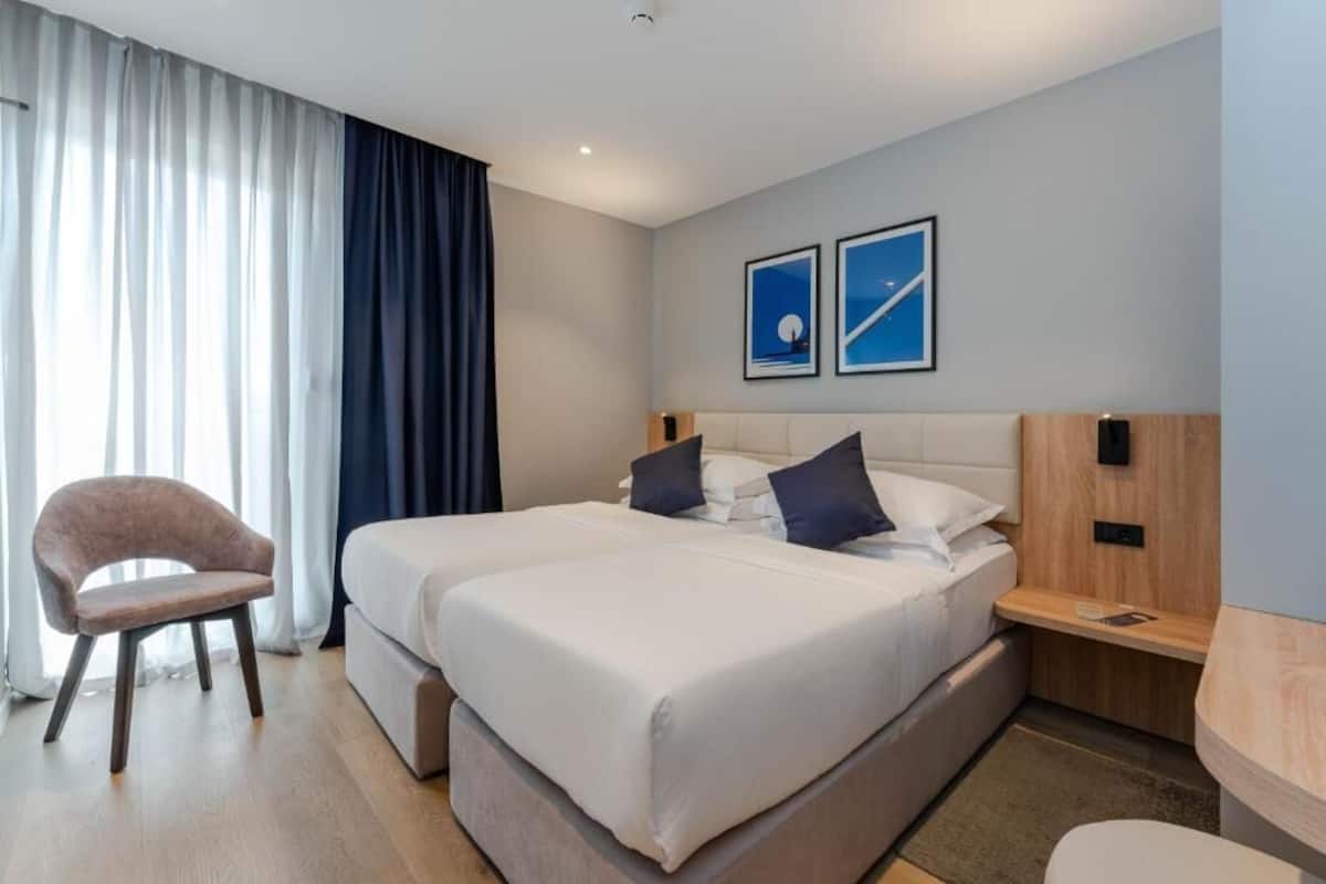 A hotel room with a bed, a chair, a bedside table, and two framed pictures on the wall.