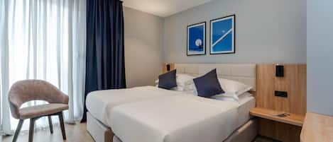 A hotel room with a bed, a chair, a bedside table, and two framed pictures on the wall.