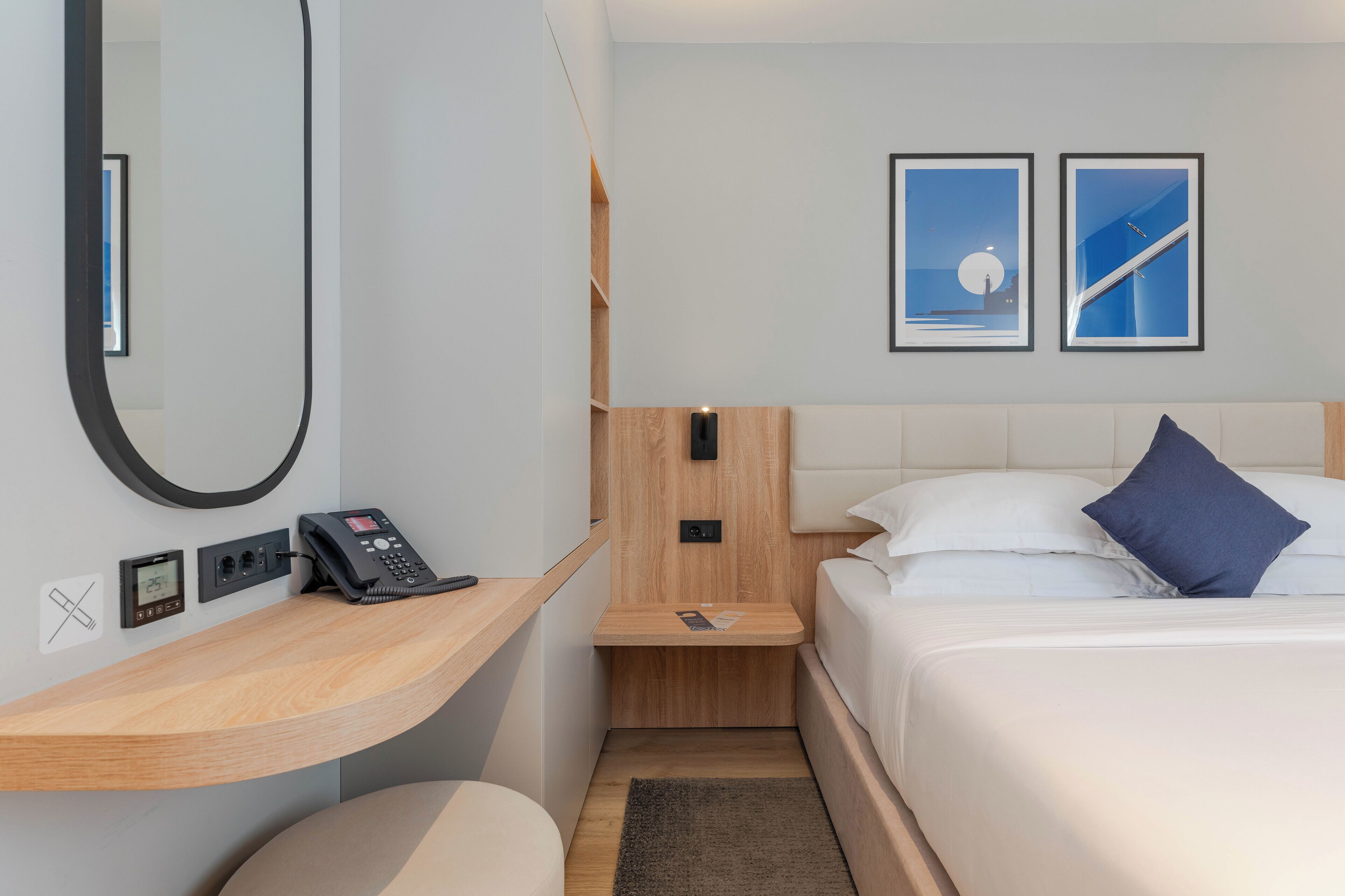 Habitación de hotel con cama, mesita de noche con teléfono, un pequeño estante de madera y dos cuadros en la pared.