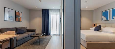 Una habitación de hotel moderna con sofá, cama, mesa de comedor y obras de arte en las paredes.