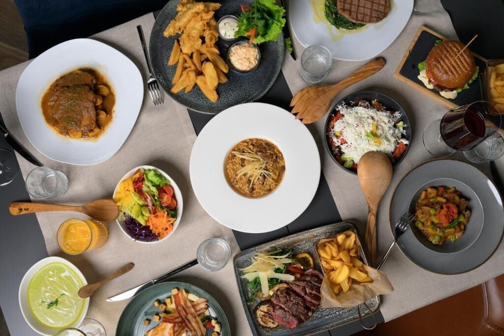 A table with various dishes including a burger, salad, and a bowl of soup.