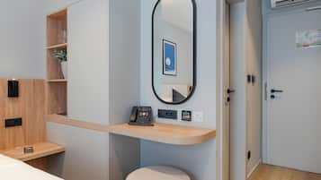 Ett modernt hotellrum med ett skrivbord i trä, en rund spegel, en telefon vid sängen och en liten pall.