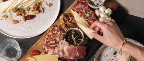Una mesa servida con varios quesos, embutidos y pan, acompañada de copas de vino tinto.