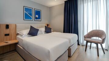 A hotel room with two beds, a wooden nightstand, a chair, and a large window with curtains.