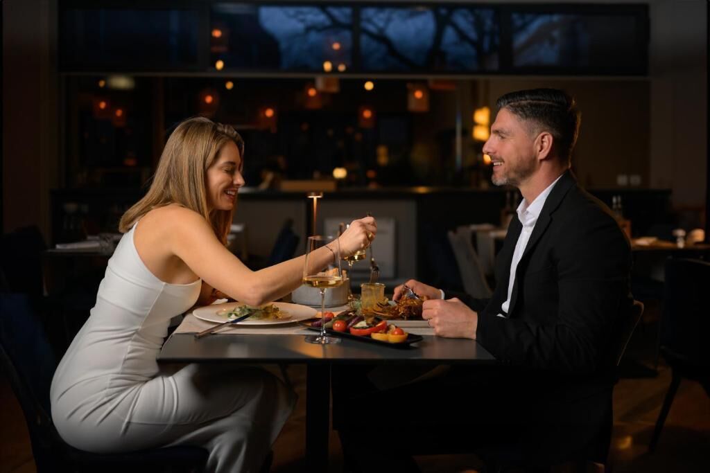 Una pareja cenando en una mesa en un restaurante con poca luz y vistas a la ciudad.