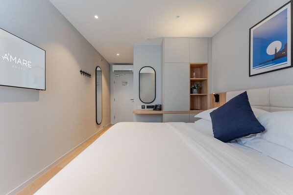 A modern hotel room with a large bed, a bedside table, a mirror, a wall-mounted TV, and a framed picture.