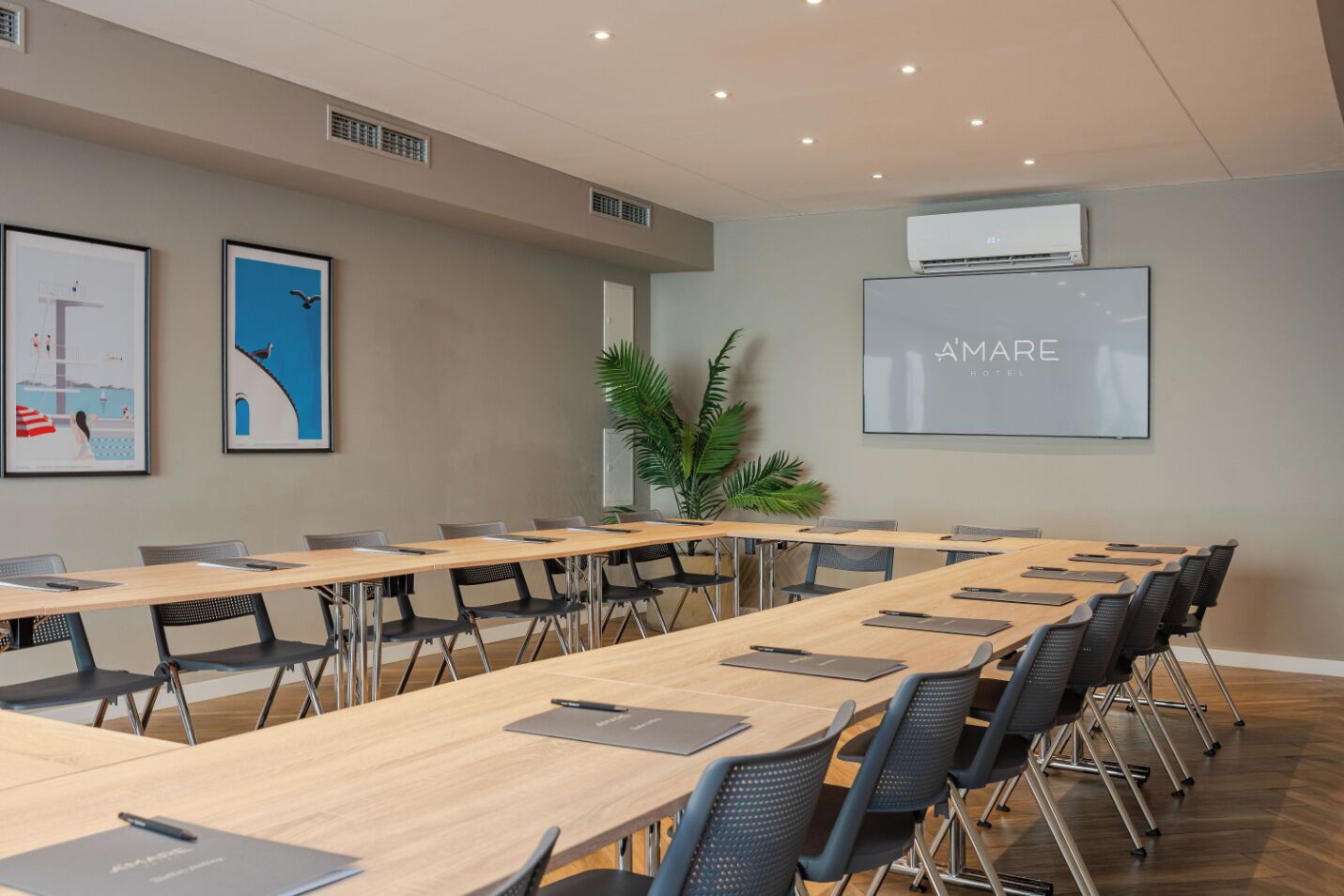 A conference room with long tables, chairs, and a large screen displaying 'AMARE HOTEL'.