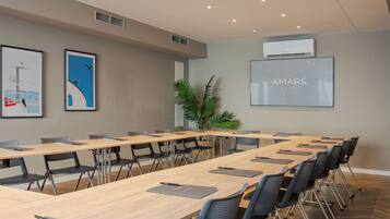 A conference room with long tables, chairs, and a large screen displaying 'AMARE HOTEL'.