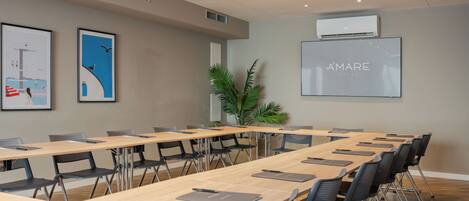 A conference room with long tables, chairs, and a large screen displaying 'AMARE HOTEL'.