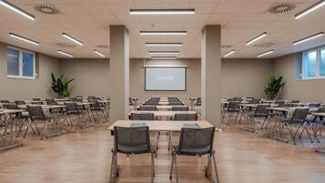 A conference room with a large screen at the front, multiple tables, and chairs arranged for meetings.