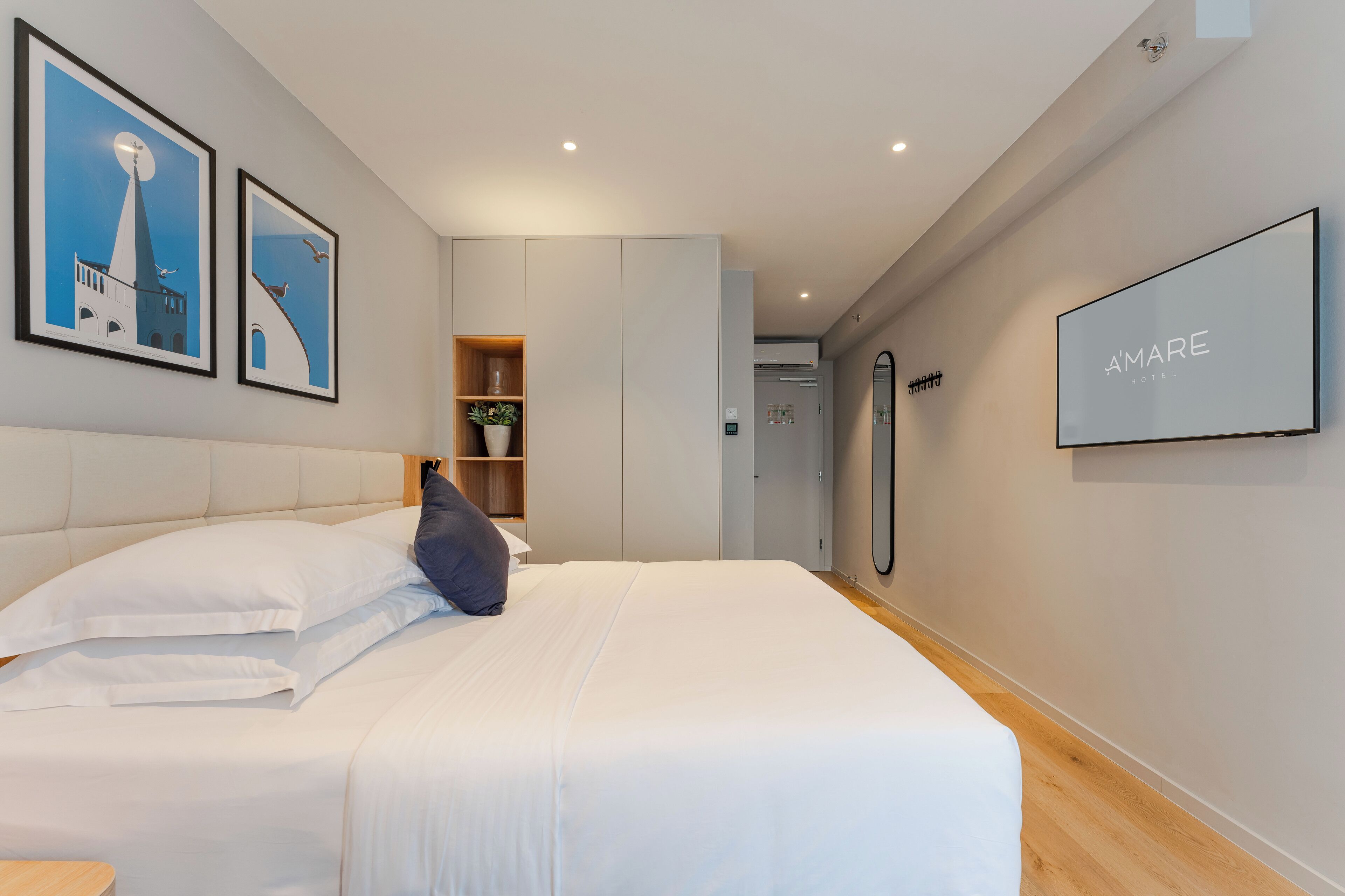 Moderni hotellihuone, jossa on suuri sänky, vaatekaappi, peili ja seinillä tauluja.