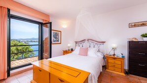 A bedroom with a bed, nightstands, a dresser, a window with a view, and a painting on the wall. - Holiday Home Es Niu with Sea View, Garden and Wi-Fi (Portocolom)