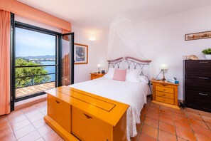 Une chambre à coucher avec un lit, des tables de chevet, une commode, une fenêtre donnant sur un beau paysage et un tableau accroché au mur.