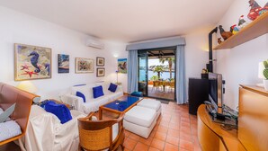 A room with a sofa, a chair, a table, a TV, and a view of the sea. - Holiday Home Es Niu with Sea View, Garden and Wi-Fi (Portocolom)