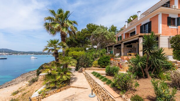 A coastal property with a stone pathway, palm trees, and a view of the sea. - Holiday Home Es Niu with Sea View, Garden and Wi-Fi (Portocolom)